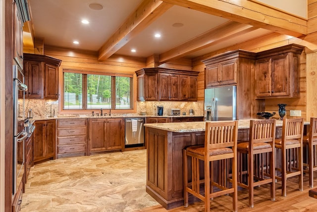 kitchen with beamed ceiling, a kitchen bar, stainless steel appliances, light stone countertops, and sink