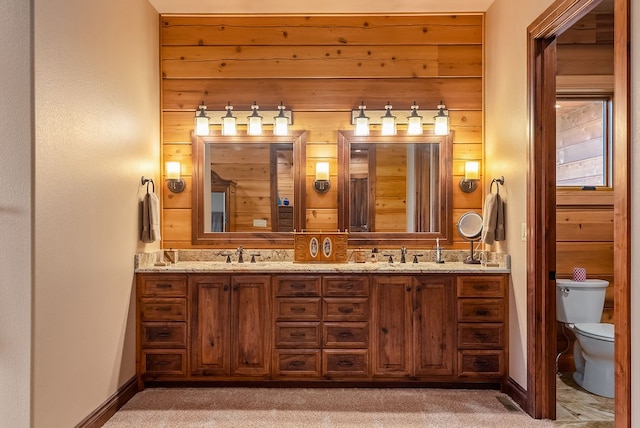 bathroom with wooden walls, toilet, large vanity, and double sink