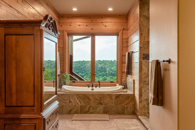 bathroom with a relaxing tiled bath, wood walls, and a wealth of natural light