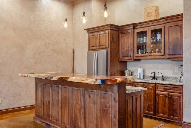 kitchen with pendant lighting, light stone counters, stainless steel fridge, light tile floors, and sink