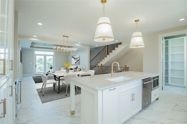 kitchen featuring white cabinets, decorative light fixtures, sink, and a center island with sink