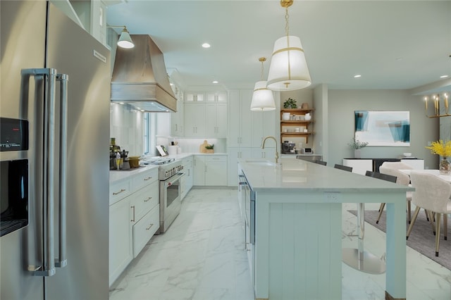 kitchen featuring high quality appliances, premium range hood, pendant lighting, white cabinetry, and a kitchen island with sink