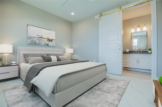 bedroom with a barn door, ensuite bath, ceiling fan, and sink