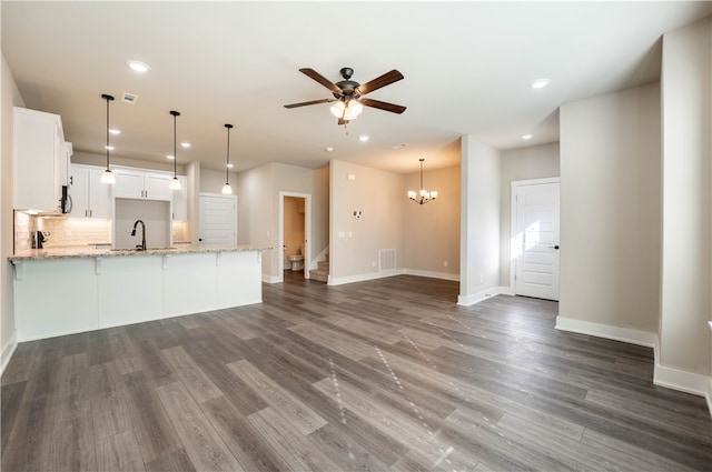 kitchen featuring ceiling fan with notable chandelier, kitchen peninsula, white cabinets, dark wood-type flooring, and light stone counters