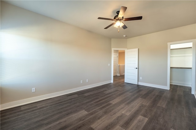 unfurnished bedroom featuring a closet, dark wood-type flooring, a walk in closet, and ceiling fan