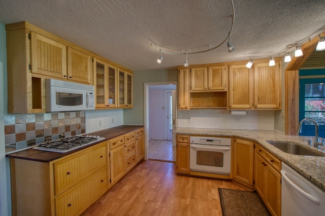 kitchen with appliances with stainless steel finishes, a textured ceiling, sink, rail lighting, and light hardwood / wood-style flooring