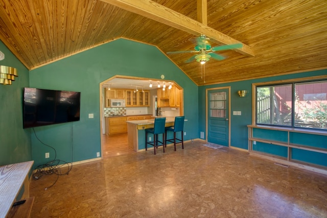 interior space featuring backsplash, a breakfast bar area, ceiling fan, lofted ceiling with beams, and wood ceiling