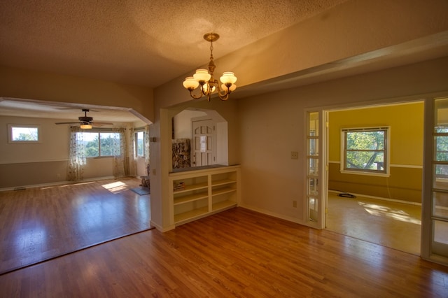 empty room with hardwood / wood-style floors, ceiling fan with notable chandelier, and a wealth of natural light