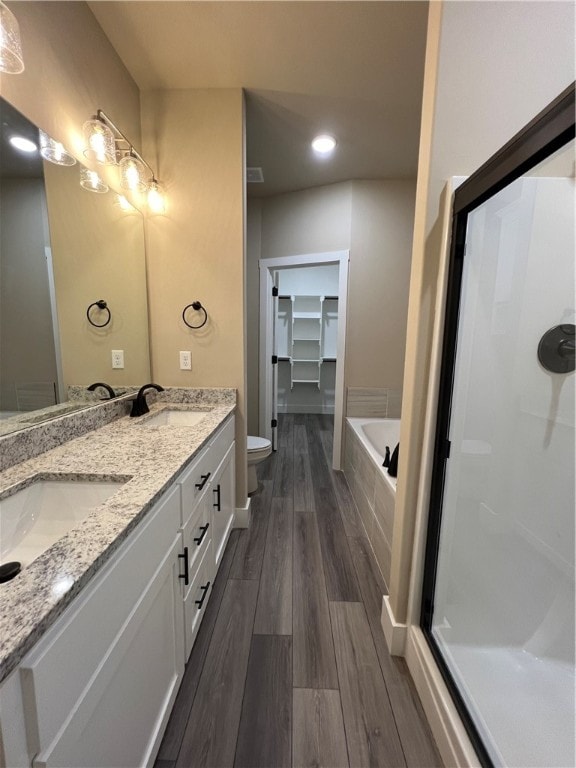 bathroom with a washtub, dual sinks, toilet, oversized vanity, and hardwood / wood-style flooring