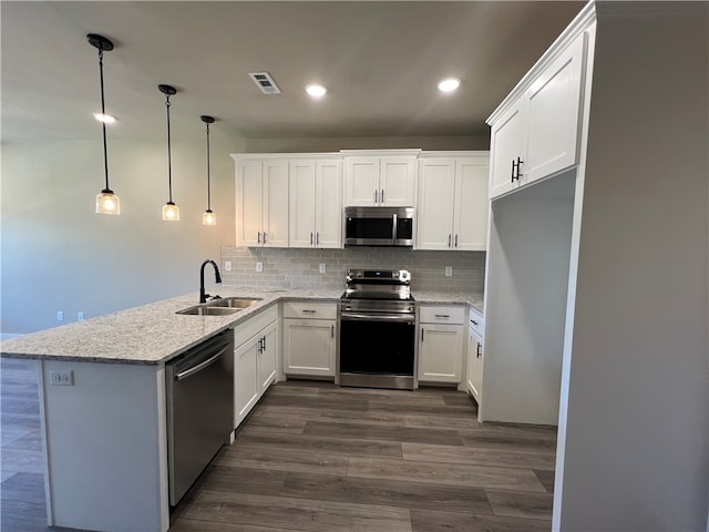 kitchen with kitchen peninsula, sink, light stone counters, white cabinets, and appliances with stainless steel finishes