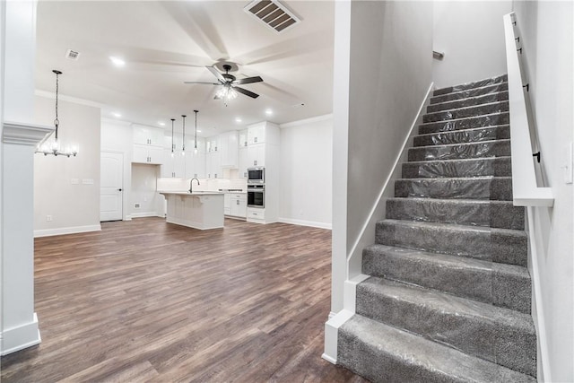 staircase featuring ceiling fan with notable chandelier, wood-type flooring, sink, and crown molding