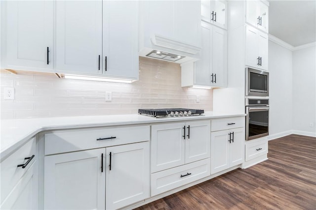 kitchen with appliances with stainless steel finishes, dark wood-type flooring, white cabinetry, and premium range hood