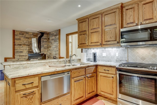 kitchen featuring kitchen peninsula, a wood stove, appliances with stainless steel finishes, light stone counters, and tasteful backsplash