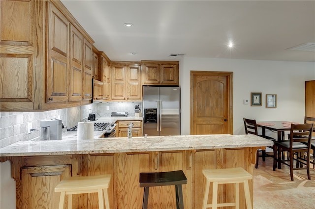 kitchen with backsplash, light stone countertops, stainless steel refrigerator with ice dispenser, and a breakfast bar