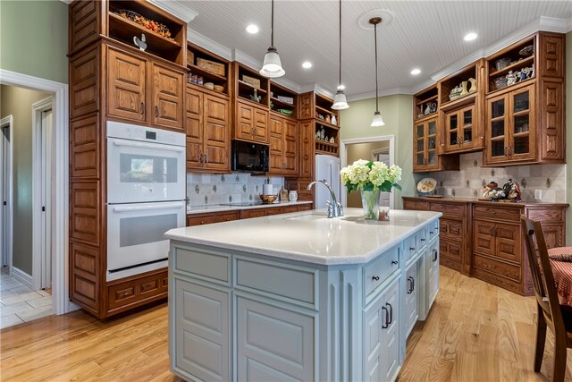 kitchen with tasteful backsplash, double oven, gray cabinets, hanging light fixtures, and an island with sink