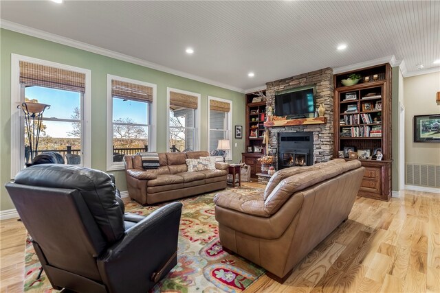 living room with a healthy amount of sunlight, light hardwood / wood-style flooring, a stone fireplace, and crown molding