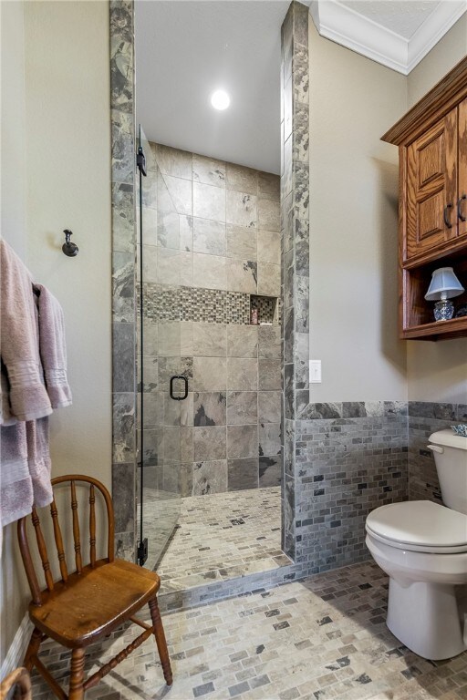 bathroom featuring toilet, tile walls, ornamental molding, and a shower with shower door