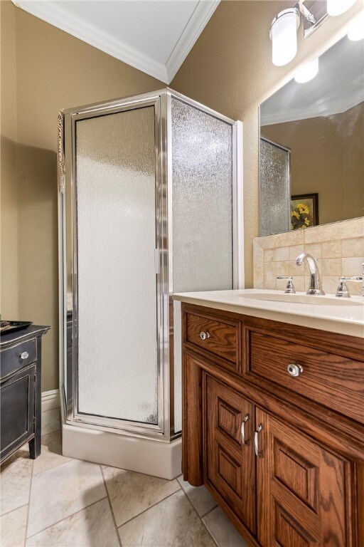 bathroom with vanity, backsplash, tile patterned floors, crown molding, and a shower with shower door