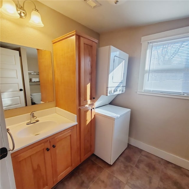 laundry area featuring laundry area, stacked washer and dryer, a sink, baseboards, and tile patterned floors