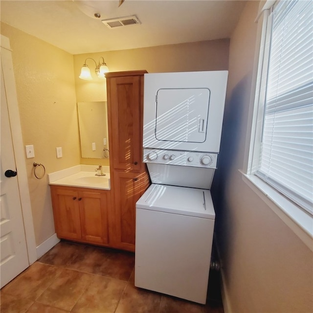 laundry area with stacked washer and clothes dryer, visible vents, a sink, baseboards, and tile patterned floors