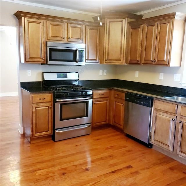 kitchen with stainless steel appliances, brown cabinetry, light wood-type flooring, and a sink