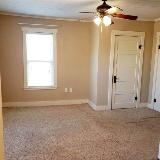 empty room featuring crown molding, baseboards, ceiling fan, and carpet flooring