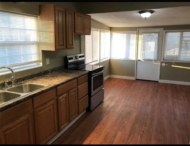 kitchen with electric range, dark wood finished floors, dark countertops, brown cabinets, and a sink