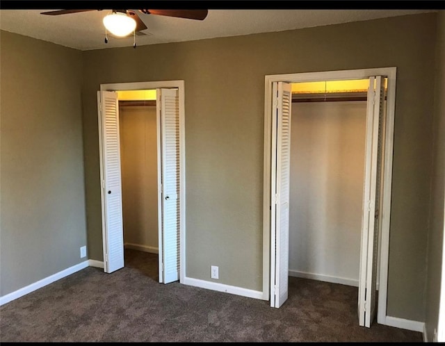 unfurnished bedroom featuring a ceiling fan, baseboards, dark carpet, and two closets