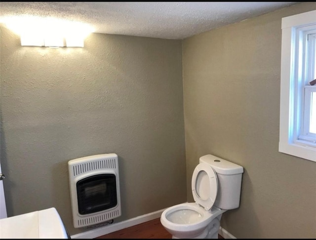 bathroom with heating unit, baseboards, toilet, and a textured ceiling