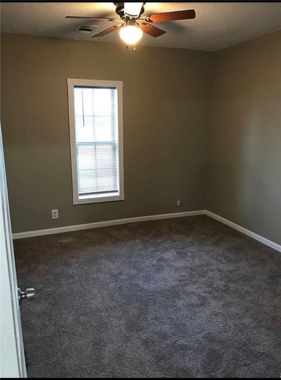 unfurnished room with a textured ceiling, visible vents, a ceiling fan, baseboards, and dark colored carpet