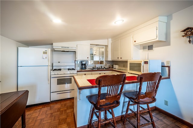 kitchen featuring white cabinets, a breakfast bar area, white appliances, and range hood