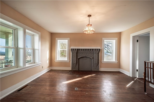 unfurnished living room with a notable chandelier, a fireplace, dark wood-type flooring, and a wealth of natural light