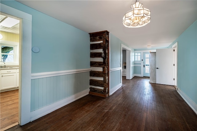 hallway featuring a chandelier, wood walls, dark wood-type flooring, and sink