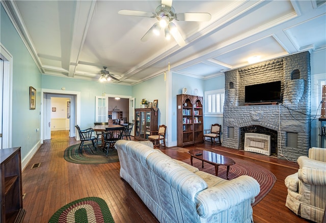 living room featuring ceiling fan, beamed ceiling, dark wood-type flooring, a fireplace, and crown molding