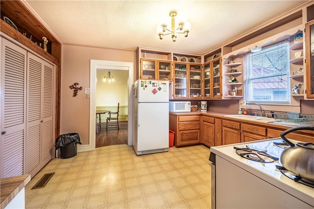 kitchen with pendant lighting, a textured ceiling, sink, a notable chandelier, and white appliances