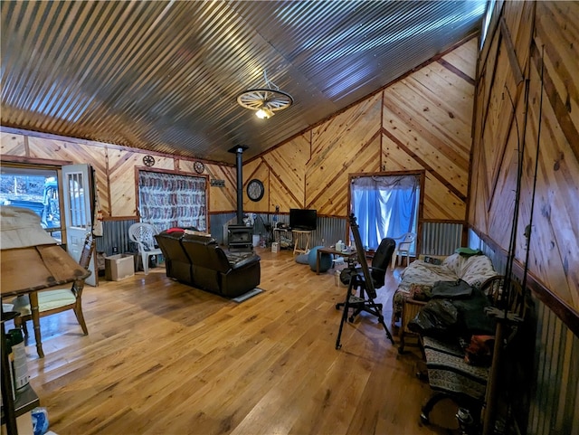 living room featuring light hardwood / wood-style flooring, a wood stove, wooden walls, and vaulted ceiling