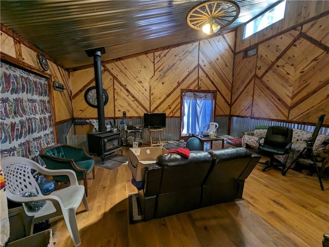 living room featuring light hardwood / wood-style floors, wooden walls, a wood stove, and lofted ceiling