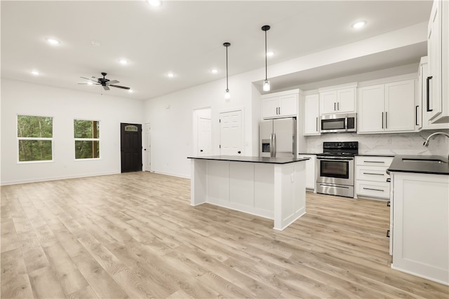 kitchen with appliances with stainless steel finishes, light wood-type flooring, a center island, ceiling fan, and white cabinetry