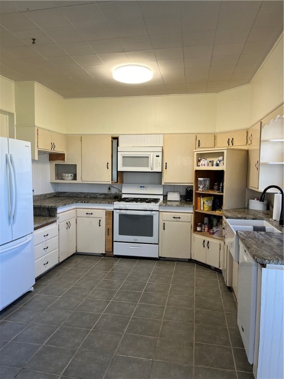 kitchen with dark stone countertops, white appliances, and dark tile floors