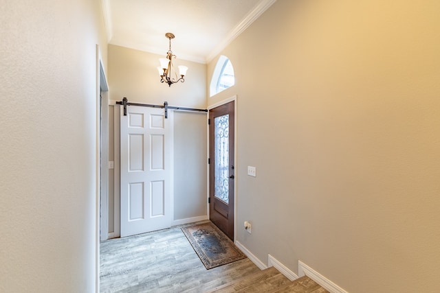 foyer with light hardwood / wood-style floors, ornamental molding, a barn door, and a chandelier