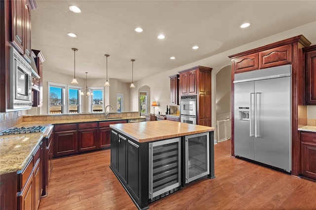 kitchen with built in appliances, a center island, wine cooler, light wood-type flooring, and sink