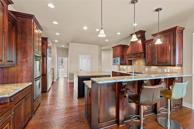 kitchen with light stone countertops, dark wood-type flooring, custom exhaust hood, stainless steel appliances, and tasteful backsplash