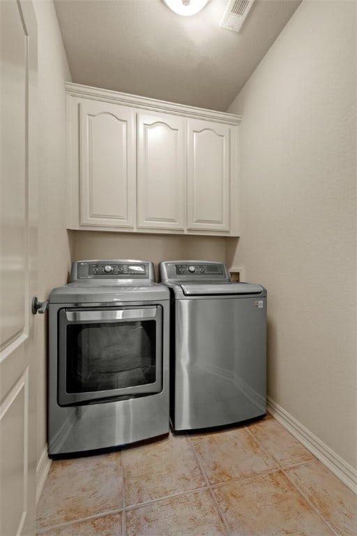 laundry area with light tile flooring, cabinets, and washer and clothes dryer