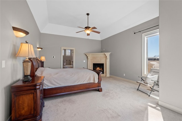 carpeted bedroom featuring ceiling fan, a tile fireplace, a tray ceiling, and vaulted ceiling