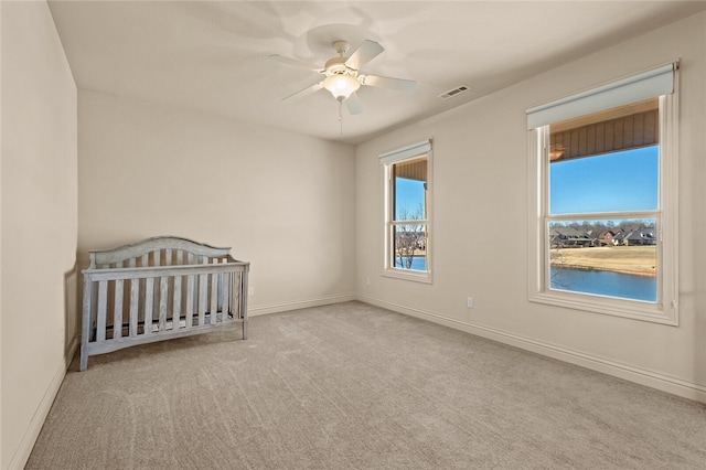 unfurnished bedroom featuring light carpet, ceiling fan, and a crib