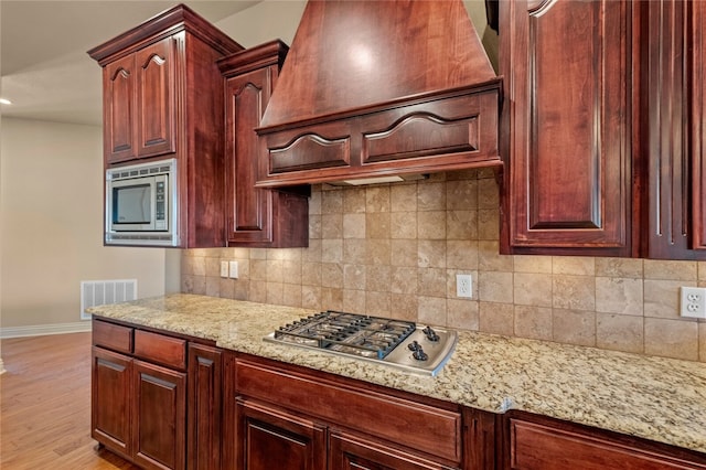 kitchen featuring backsplash, light hardwood / wood-style floors, premium range hood, and appliances with stainless steel finishes