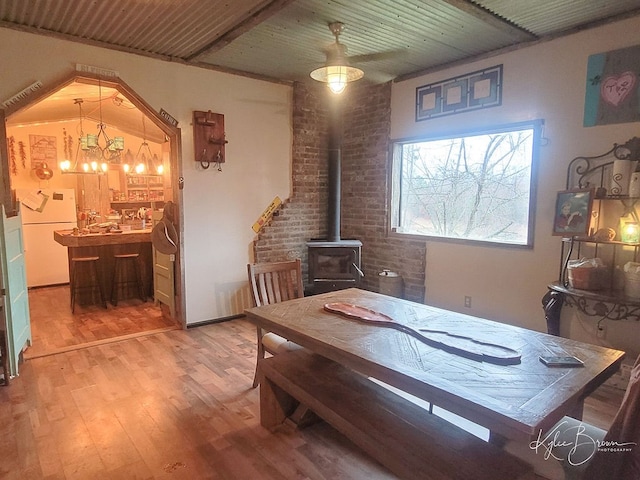 dining space featuring brick wall, hardwood / wood-style flooring, an inviting chandelier, and a wood stove