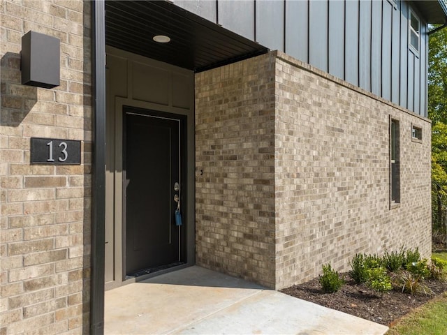 doorway to property featuring board and batten siding and brick siding