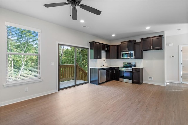 kitchen featuring light wood finished floors, stainless steel appliances, dark brown cabinets, light countertops, and a sink