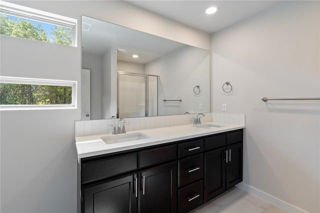 full bathroom featuring double vanity, a stall shower, a sink, and baseboards